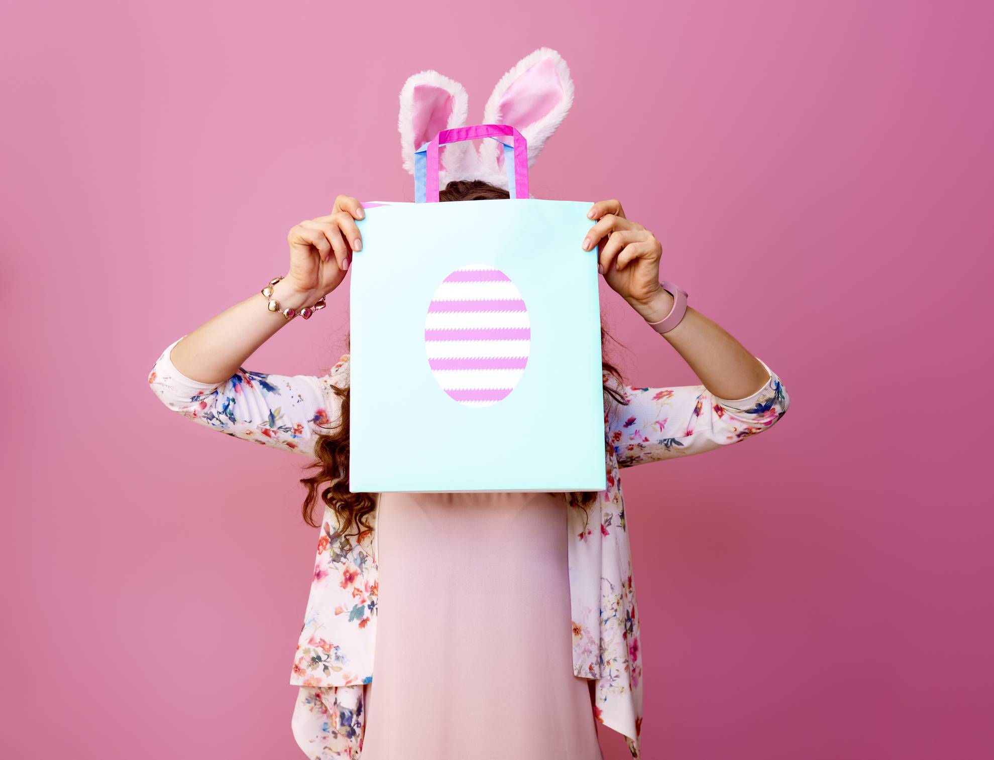 young woman on pink background hide behind Easter shopping bag